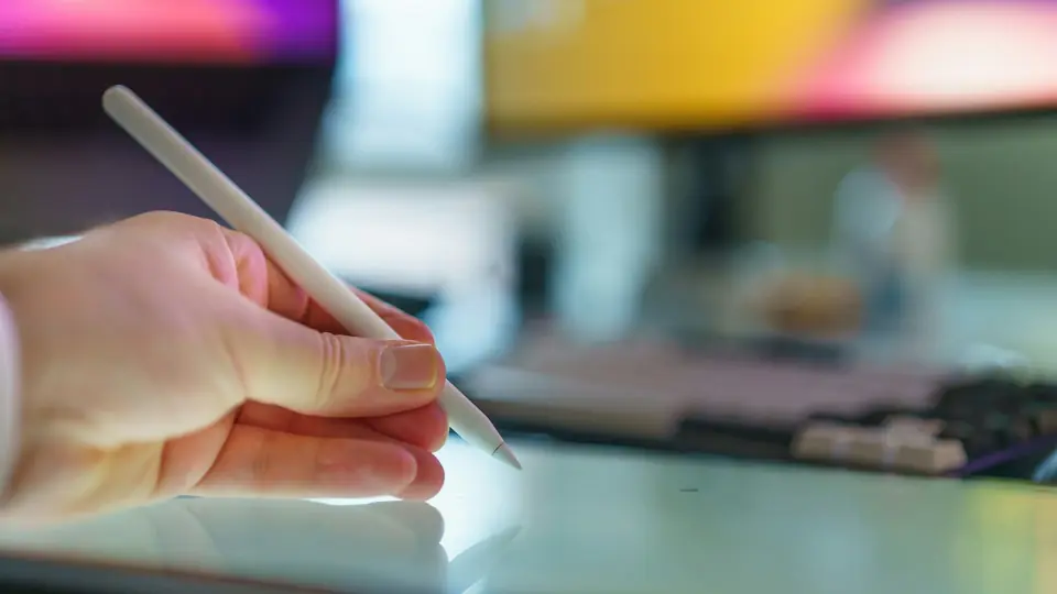 Eine Hand hält einen Stift über einem Tablet; Kontextfoto zu einem Artikel über Bildbearbeitungswerkzeuge.