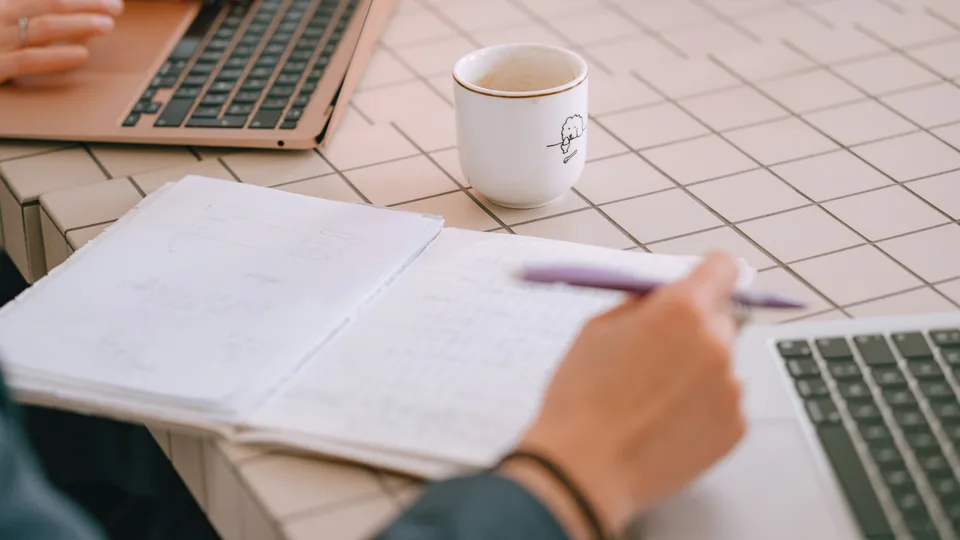 Zwei Kolleginnen oder Kollegen arbeiten gemeinsam an Laptops und planen Arbeitsabläufe.